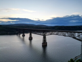 Obraz premium view of walkway over the hudson at sunset (tall former railroad bridge over the hudson river in poughkeepsie new york) part of empire state trail and hudson valley rail cycling pedestrian path