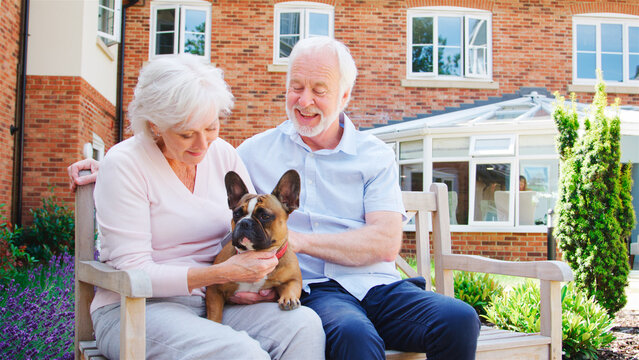 Retired Couple Sitting On Bench And With Pet French Bulldog In Assisted Living Facility