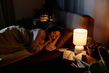High angle shot of relaxed adult woman napping calmly while night lamp illuming bedroom