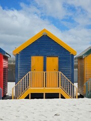 Naklejka premium Colorful wooden beach huts lining sandy muizenberg coastline, framing azure sky and pristine white landscape near cape town, south africa