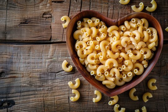 Uncooked Elbow Macaroni Pasta in a Heart Shaped Wooden Bowl on Rustic Dark Wood Tabletop