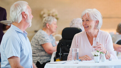 Senior Couple Waiting For Meal To Be Served In Dining Room Of Retirement Home