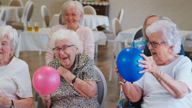Carer Leading Group Of Seniors In Activity With Balloons In Retirement Home