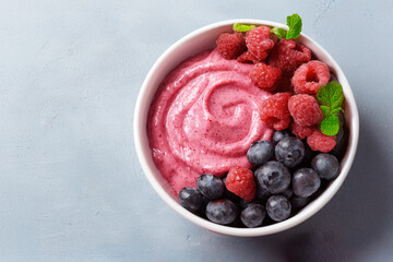 A vibrant bowl of berry smoothie topped with fresh raspberries, blueberries, and a sprig of mint, perfect for a refreshing snack or breakfast.