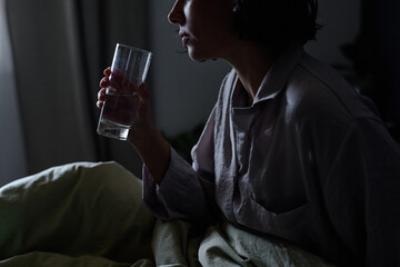 Medium close up of unrecognizable woman sitting in bed and holding polished glass full of water in...