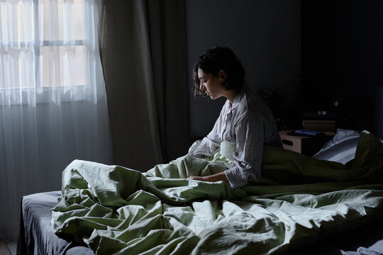 Brunette woman with closed eyes sitting on bed, she suffering from parasomnia