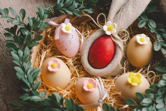 A decorative nest for Easter displays colorful eggs with floral accents, nestled in soft straw and surrounded by green leaves on a textured blanket. Easter concept
