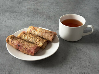 Russian breakfast. Black tea in a white cup and stuffed pancakes on gray background.