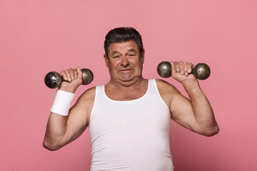 Mature man in white tank top tensely lifting dumbbells. Isolated.