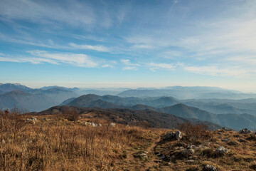 vista panoramica in alta quota su un ambiente naturale tra le montagne e le colline lungo il confine tra Italia e Slovenia, di mattina, a fine autunno, con cielo leggermente nuvoloso