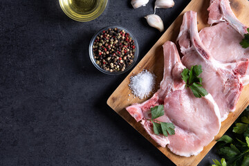 Fresh uncooked pork chops on cutting board and black stone background. Top view