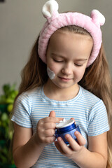 Young caucasian girl applying face cream with pink headband
