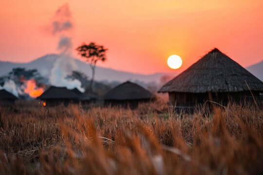 A peaceful Zulu village at dawn, with smoke rising from thatched huts and a pink sky glowing in the background