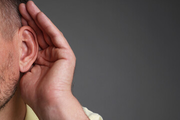 Man showing hand to ear gesture on grey background, closeup. Space for text