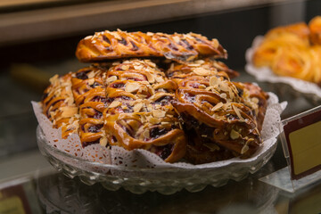 A tempting assortment of freshly baked pastries is arranged on a delicate glass platter. The treats are adorned with almonds and have a golden-brown crust, inviting customers to indulge.