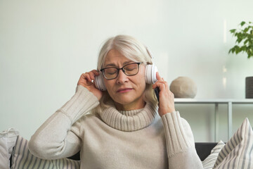 Senior woman listening to calming music with headphones at home