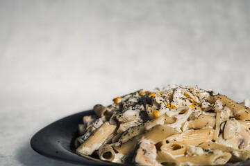 Chicken penne pasta on a black plate with ample copy space and focus on texture.