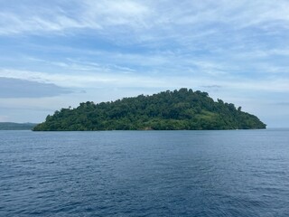 Naklejka premium Tropical green island surrounded by calm blue ocean under clear sky.