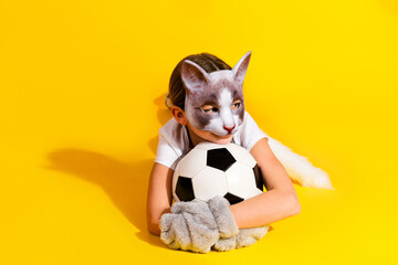 Young girl in a realistic cat mask holding a soccer ball against a yellow background, embracing playful cosplay and creativity