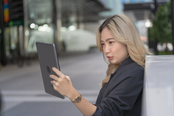 Professional woman holding a tablet in a modern urban setting surrounded by skyscrapers, showcasing confidence, technology, and adaptability in a sleek and innovative environment.