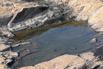 Water has collected on the rock's surface. The rock is a brown color and smooth. In hilly areas, during monsoon season, rain water gets collected in these rocks. Small water pond on top of the rock.
