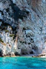 Landscape with a blue-green sea and a small beach with pebbles under a rock. Greece