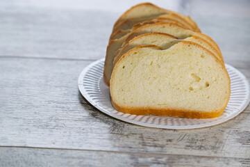 Slices of bread on a white plate against a simple wooden surface, disposable tableware with sliced bread on a kitchen table, representing abundance and poverty