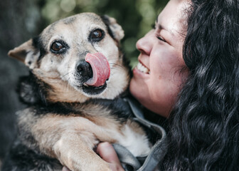 A close-up view of a young Latina kissing her black and beige dog. The dog sticks out its tongue in a graceful gesture evidencing mutual affection. A perfect display of love for dogs in one image.