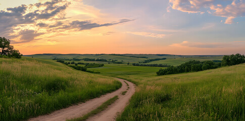 Fototapeta premium A beautiful sunset over the countryside, with green wheat fields and an old country road leading to it