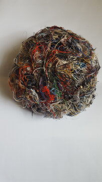 A ball of scrap cotton thread used for sewing is rolled into a multicolored ball.  