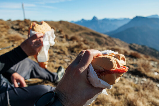 mangiare un panino in cima ad una montagna. dettagli sulle mani di due uomini adulti caucasici irriconoscibili che mangiano dei panini col salame in cima ad un monte, di giorno
