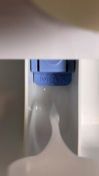 Vertical 4K video. Top view. Fabric softener and detergent is poured into washing machine cell. Limit mark with text MAX. Limiter. White liquid. Concept of laundry, washing bed linen, clothes, load