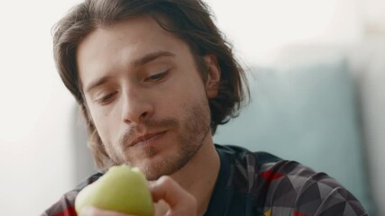 A young man takes a moment to enjoy a fresh fruit snack while working out at home, focusing on maintaining a healthy lifestyle. He looks relaxed and content.