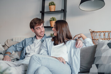 Young happy couple having fun talking laughing relaxing at home on couch, boyfriend embracing...