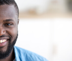 Closeup shot of happy young african man in blue shirt looking at camera and smiling, portrait of positive black bearded guy in traditional african costume, selective focus with free space. High
