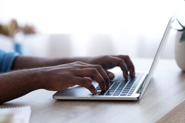 Selective focus on male hands typing on laptop keyboard, cropped, side view. African american businessman sending emails to clients or assistant. Modern technologies and business concept. High quality