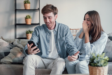 Excited millennial husband and wife relax on couch in kitchen feel euphoric win lottery online on...