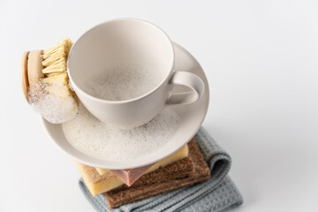 Stack of sponges, rags, natural soap and clean white cup with brush on white background. Eco-friendly dishwashing concept