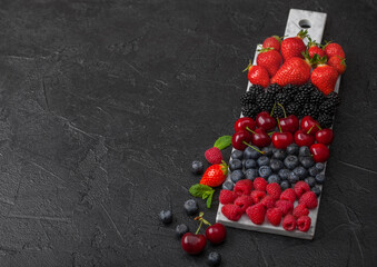 Fresh organic summer berries mix on white marble board on dark kitchen table background. Raspberries, strawberries, blueberries, blackberries and cherries. Space for text