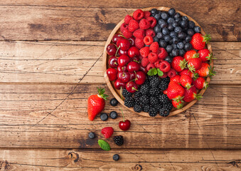 Fresh organic summer berries mix in round wooden tray on light wooden table background....