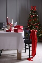 Christmas table setting with stylish dishware, glasses and burning candles in festive decorated room