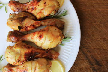 BBQ Grilled Chicken Drumsticks on white plate. Grilled chicken legs with mustard on wooden table served on white plate with rosemary. BBQ dinner background

