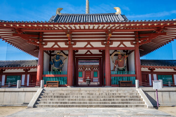 Obraz premium Shitennoji Temple's Chumon Middle Gate (Niomon) showcases ornate architecture, a staircase, and two guardian statues. Red and teal colors stand out against the blue sky.