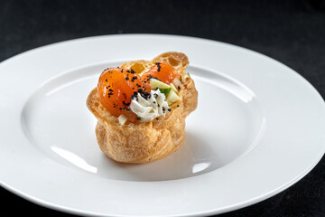 Fresh golden profiterole with pieces of red fish, salad and cream. Plated on a white plate.