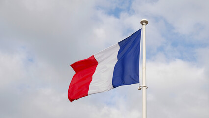 French national flag waving on cloudy sky background. The flag on a flagpole flutters in the wind. The image conveys the spirit of France: freedom, equality, fraternity.