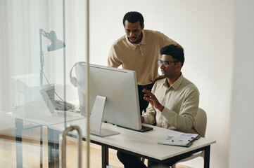 Partners discussing online presentation on computer monitor during teamwork in office