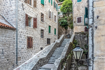 Narrow stone steps leading between historic buildings in Kotor, Montenegro, showcasing traditional architecture with shutters and greenery. Cats rest on the steps, adding a quaint touch to the scene