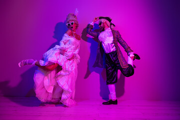 Elegant couple in period costumes on a neon violet background dancing in a playful and glamorous pose