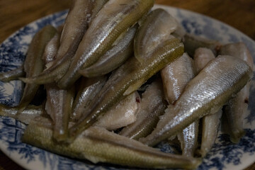 Raw smelt fishes on a plate. Small raw fish, snetok or smelt on a plate.  A portion of raw fresh fish on a plate. Before frying. smelt or horse mackerel. Close-up