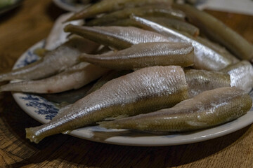 Raw smelt fishes on a plate. Small raw fish, snetok or smelt on a plate.  A portion of raw fresh fish on a plate. Before frying. smelt or horse mackerel. Close-up